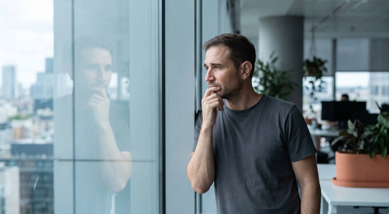 Matthias May steht nachdenklich an einem Bürofenster, seine Spiegelung ist schwach im Glas sichtbar (KI-generiertes Bild)